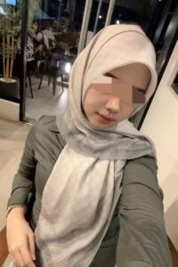 Elegant Malay Escort in KL, reflected in a mirror, wearing a hijab and a black dress. Girl Service.
